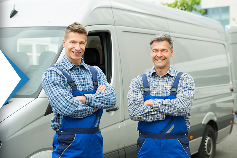 two men in blue overalls standing by service van